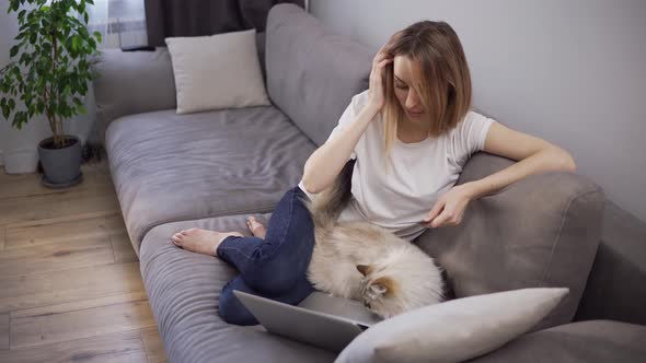 Blonde Woman Sitting on a Sofa Pays for Purchases Online with a Credit Card and Laptop