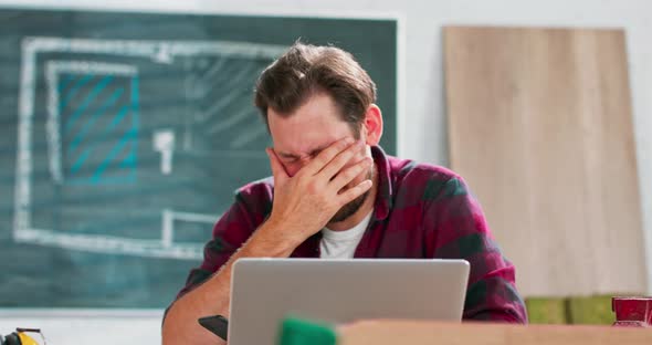 Tired Young Craftsman Sits at a Workbench in His Carpentry Workshop A Worried Carpenter Analyzes the