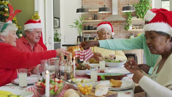 Group of happy diverse senior friends in santa hats making a toast at christmas dinner table at home
