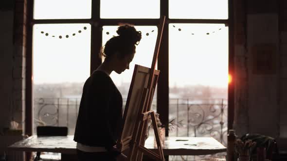 Young Inspired Professional Female Artist Puts Cancas on Easel Takes Palette with Paint on It and