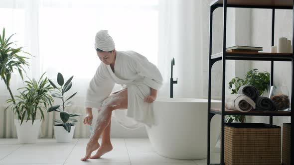 Slow Motion of Feminine Student in Bathrobe Shaving Legs in Bathroom Alone