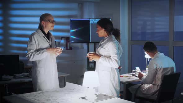 Mixed Race Female Engineers in White Coats Discussing Something in Modern Lab