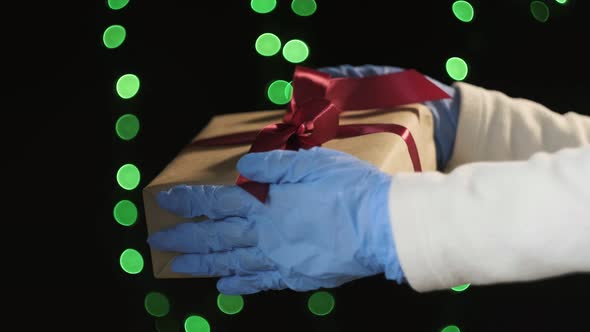Closeup on Hands in Blue Protective Gloves Holding Gift Box with Red Ribbon
