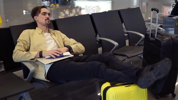 A Bearded Man in Yellow Shirt Sleeping Holding Legs on the Yellow Suitcase Holding His Stuff in the