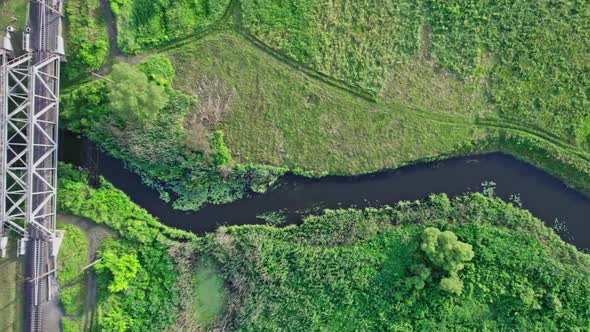 Small River Flows Smoothly Between Green Fields and a Railway Bridge