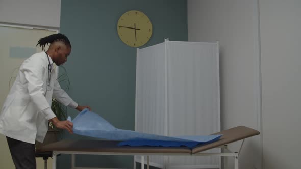 Male Physician or Nurse Covering Diagnostic Bed with New Sheet Indoors