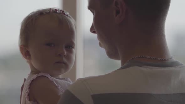 Handsome Man Holding Little Baby Girl in His Arms in Front of Window Close-up. The Joys of