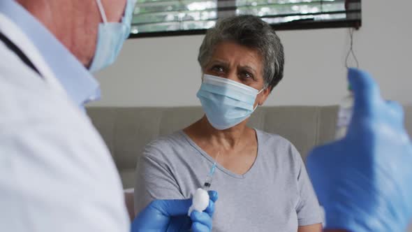 Caucasian male doctor preparing vaccination for senior african american woman at home