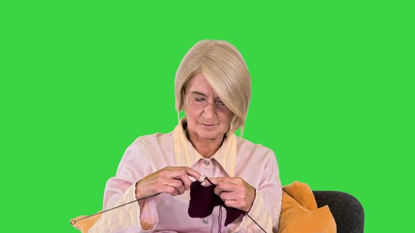 Senior Lady Knitting Sitting on a Chair on a Green Screen, Chroma Key