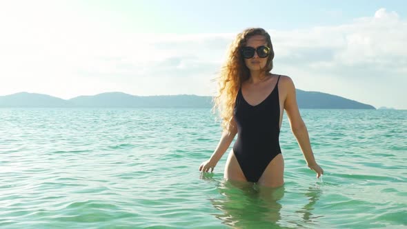 Curly Haired Model Wearing a Black One Piece Swimsuit and a Sunglass