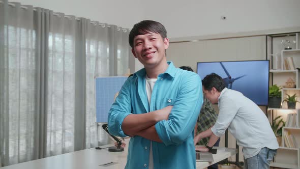 Smiling Asian Man Engineer Crossing His Arms To Camera While His Colleagues Are Discussing Working