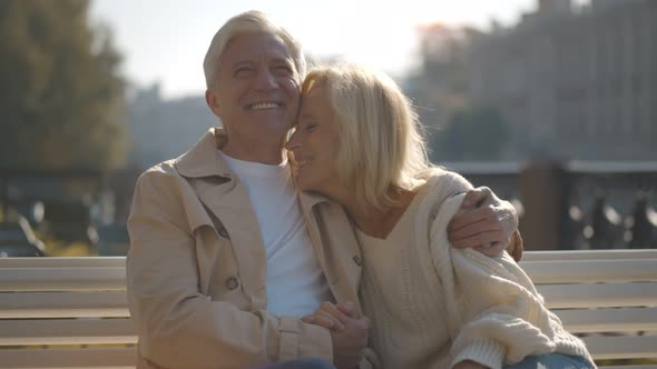 Happy Senior Couple Holding Hands and Hugging with Smile Sitting on Bench