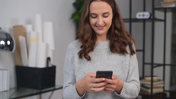 Smiling Young Woman is Using Smartphone in the Office