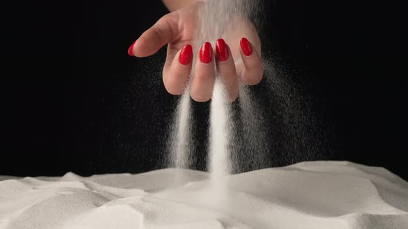 Stream of White Sand Pours Into Palm of Woman and is Spilling Through Her Fingers on Black