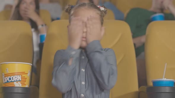 Portrait of Pretty Frightened Little Girl Closing Eyes with Hands in Movie Theater. Charming Cute