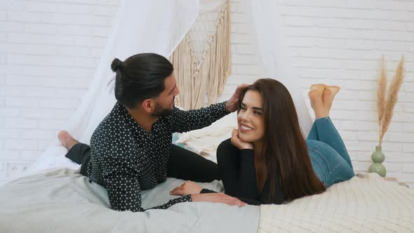 Cute Couple Looking at Each Other While Layong on the Bed Smiling Broadly and Enjoying Time Together