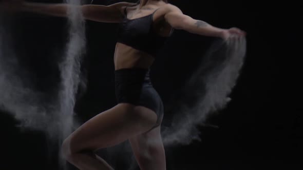 Girl with Ideal Body Throws Dust in Studio on Black Background. Slow Motion