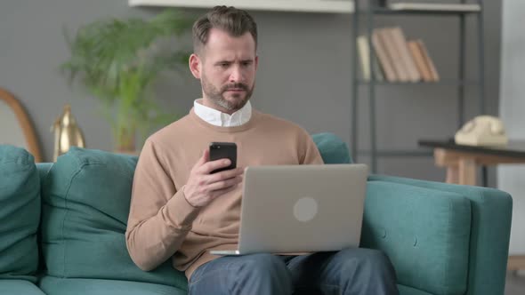 Man with Laptop Using Smartphone on Sofa