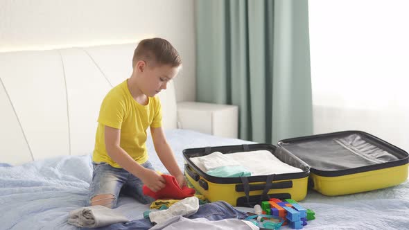 Little Boy Is Putting Clothes in a Suitcase for a Vacation Trip