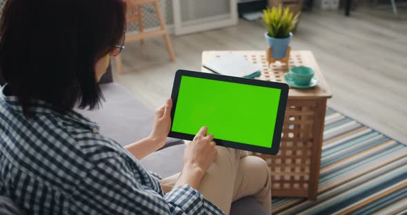 Person Holding Tablet Touching Green Mock-up Screen Using Device at Home