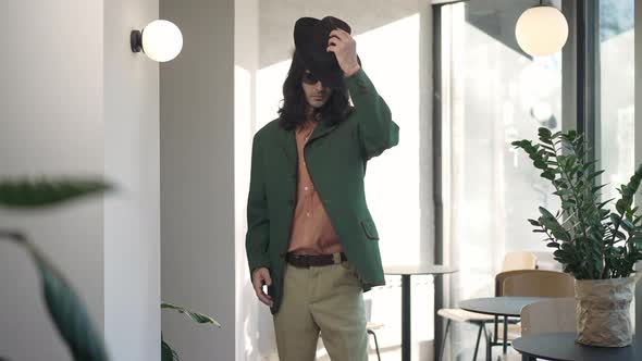 Stylish Confident Man in Sunglasses Putting on Hat in Slow Motion Standing Indoors in 1980s