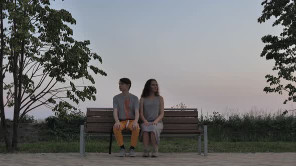 Young Couple Sitting on a Bench Facing the Camera