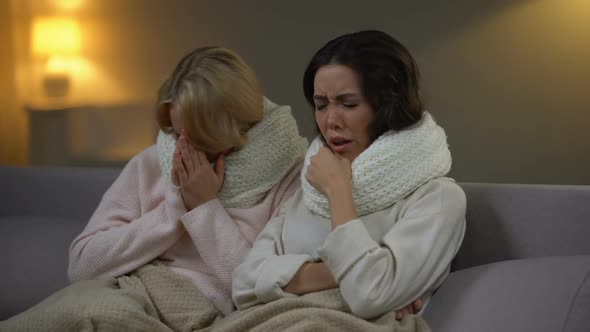 Two Sick Girls Sitting With Scarfs in Bed and Sneezing