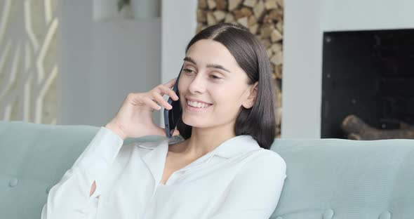 Young Woman Business Entrepreneur in Casuals Sitting on Sofa and Talking Over Smartphone at Home