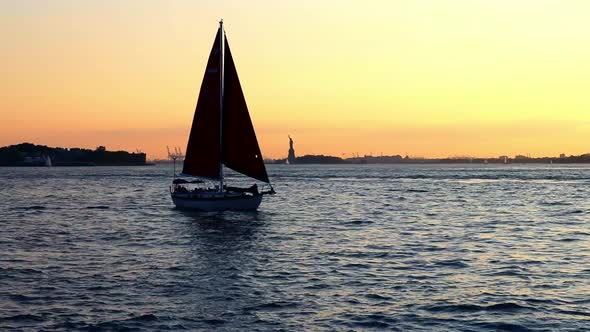 Sailboat passing in front of Statue of Liberty at sunset