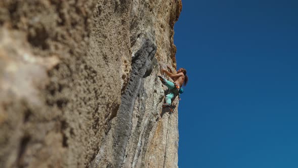 Bottom View of Muscular Strong Man Rock Climber Climbs on Vertical Cliff on Rock Wall on Blue Sky