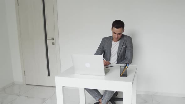 Male Student in a Suit Studies on Laptop Remotely in Room with a Light Interior