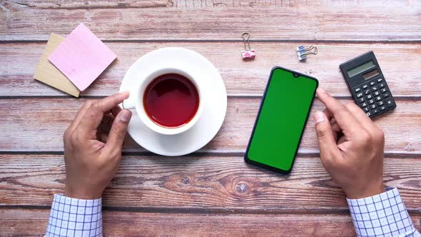 Top View of Man Hand Holding Smart Phone and Drinking Tea