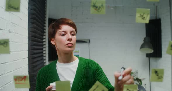 Young Woman is Engaged in Planning Using Glass Board Working Alone in Office