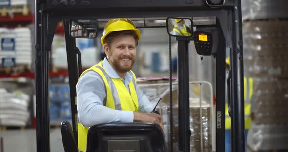 Portrait Young Male Warehouse Worker Sitting in Forklift Truck and Smiling at Camera