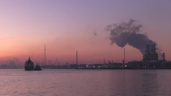 a cargo ship, assisted by a tugboat coming in at dawn at the port of Antwerp and its industry