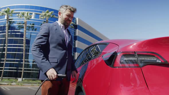 Senior Businessman is Plugging in Power Cord to Electric Car at Business Office