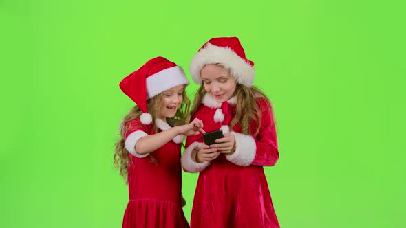 Two Baby Girls Look at the Pictures on the Phone and Laugh. Green Screen. Slow Motion