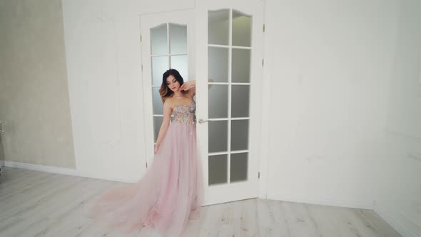 Beautiful bride in wedding dress is standing near the door in the light room.