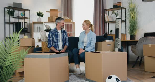 Couple Talking on the Couch Between Themselves when their Two Kids Jumping out Carton boxes