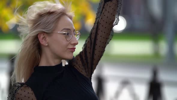 Portrait of an Attractive Blonde Girl with Glasses Walking Along a City Street on an Autumn Day