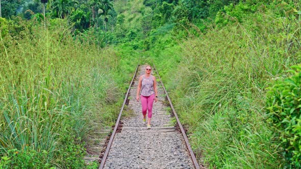 Female walking on empty train railway surrounded by tropical grass and trees