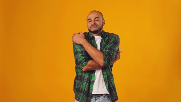 Young African American Man Hugging Himself and Feeling Comfortable Against Yellow Background