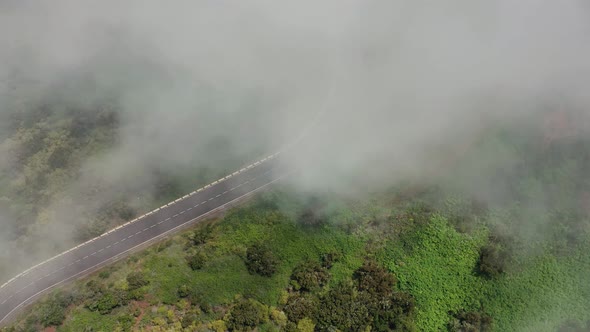 Flying Through the Clouds Over a Mountain Road Surrounded By Green Vegetation