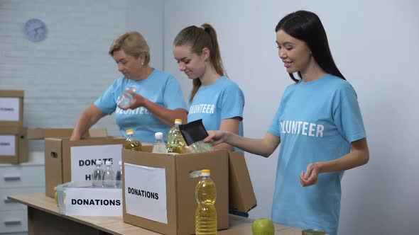 Joyful Women in Volunteer T-Shirts Putting Canned Food Boxes Provision Donation