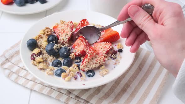 Eating granola with berries with spoon.