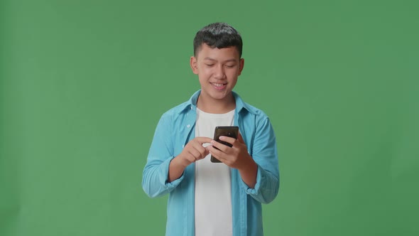 Smiling Young Asian Boy Using Mobile Phone In Green Screen Studio