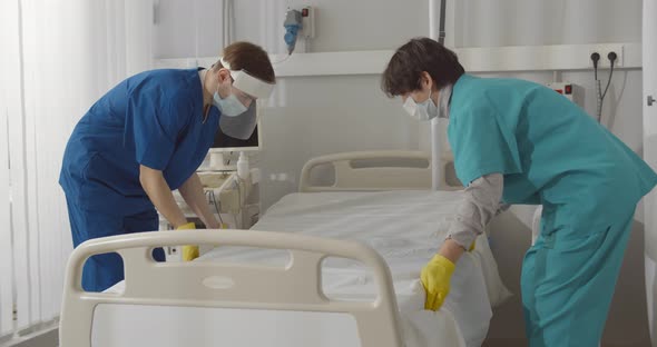 Medical Staff Changing Linen of Bed in Empty Hospital Ward