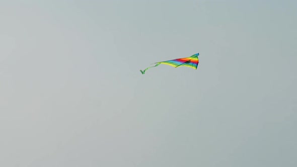 Colorful Kite with Wide Stripes and Tail Flies in Clear Sky