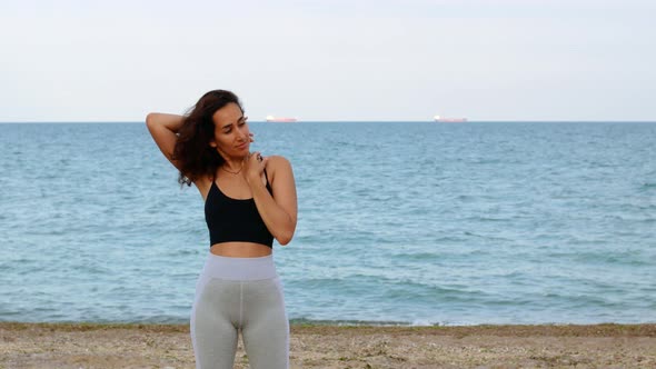 Beautiful young tanned sports girl in sportswear stands on the ocean.