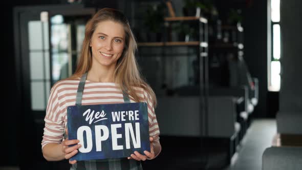 Portrait of Attractive Blond Waitress Holding Open Sign in New Cafe Smiling